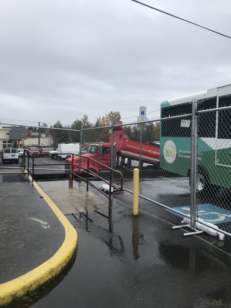 A bus is parked in the rain near a fence.