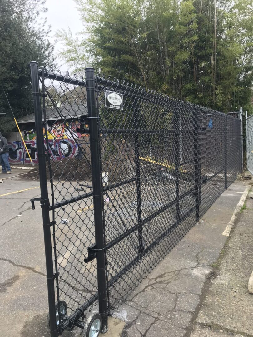 A black chain link fence with people walking around.