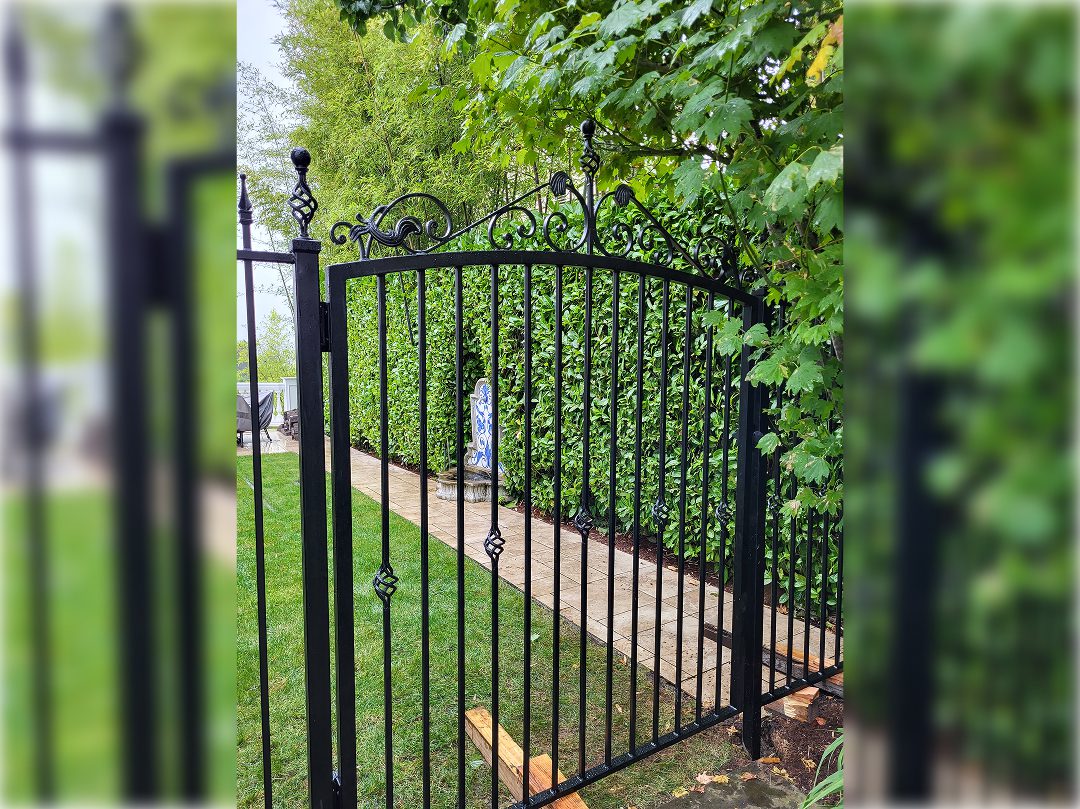 A black metal gate in the middle of a garden.