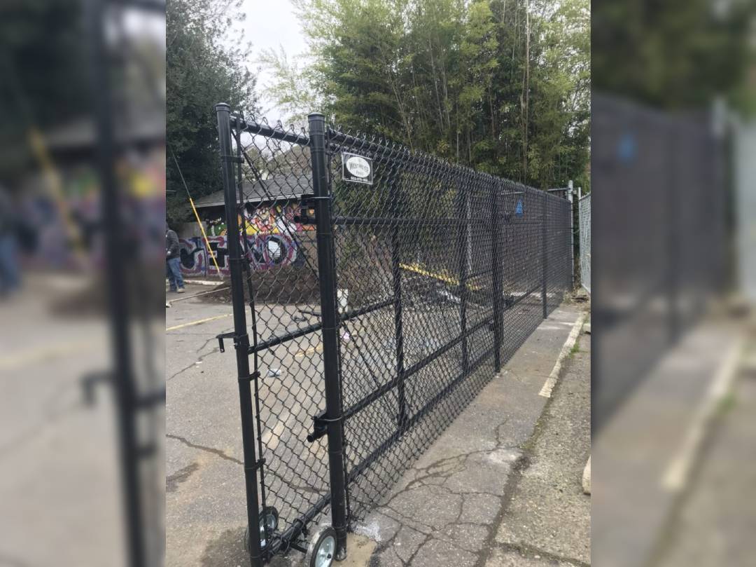 A chain link fence with a gate and some trees