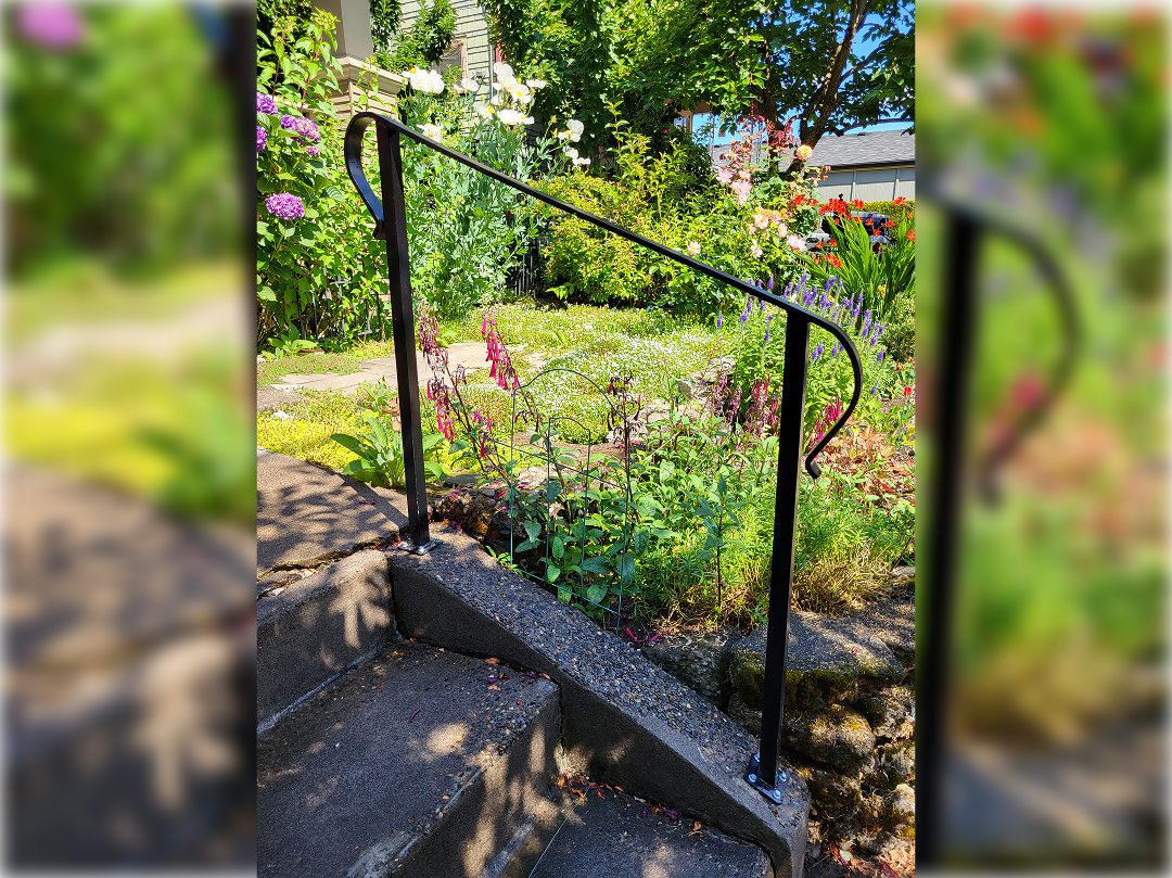 A metal railing on the side of steps in front of flowers.